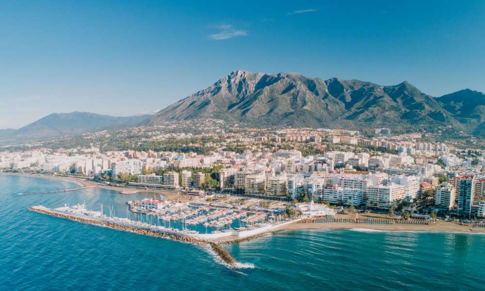 Vibrant coastal cityscape with a marina, modern high-rise buildings, and mountain views, highlighting a dynamic real estate network in a prime location.